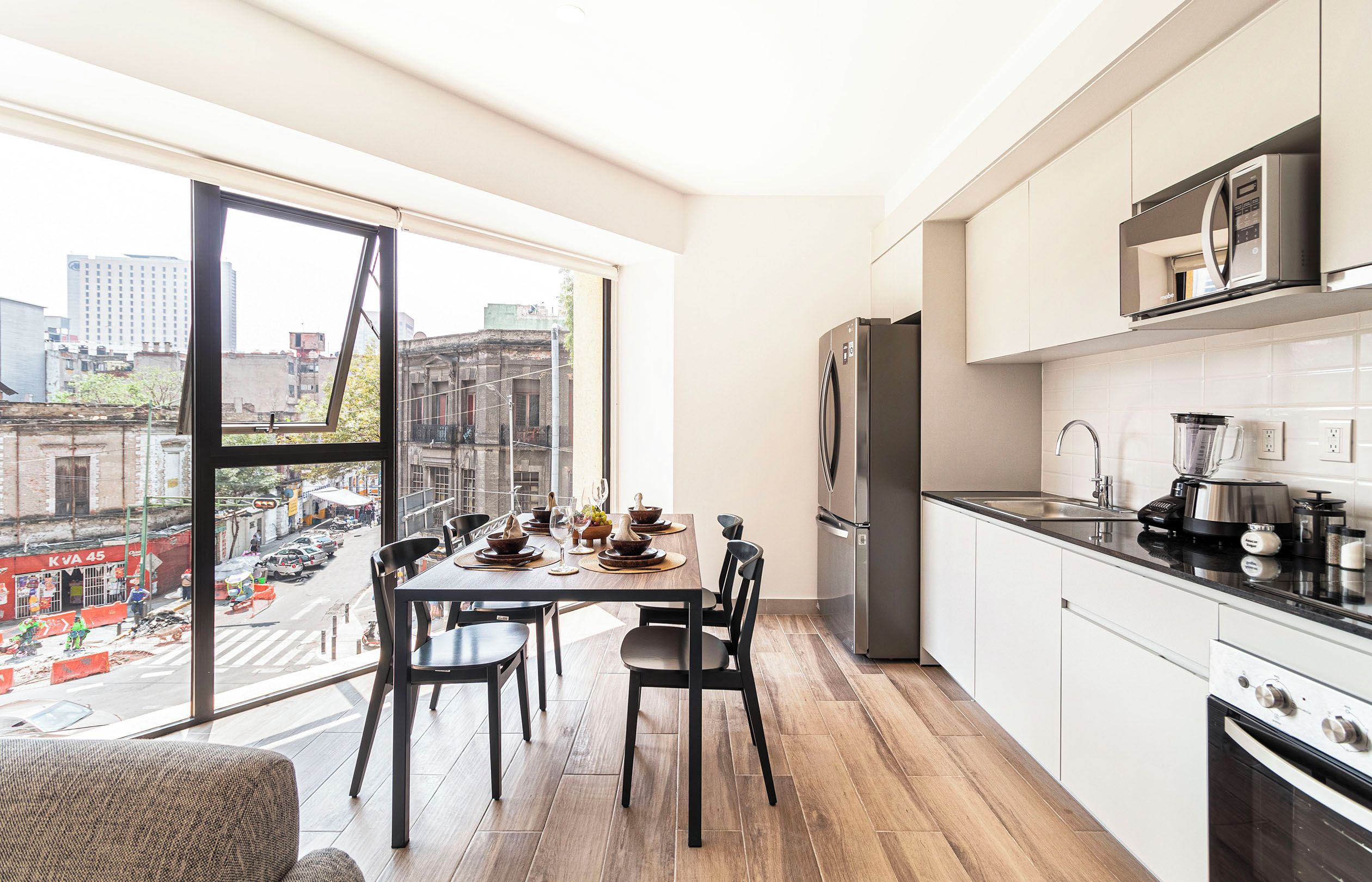 A modern kitchen with a large window, a dining area with a table set for four, and a view of the cityscape.
