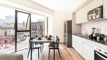 A modern kitchen with a large window, a dining area with a table set for four, and a view of the cityscape.