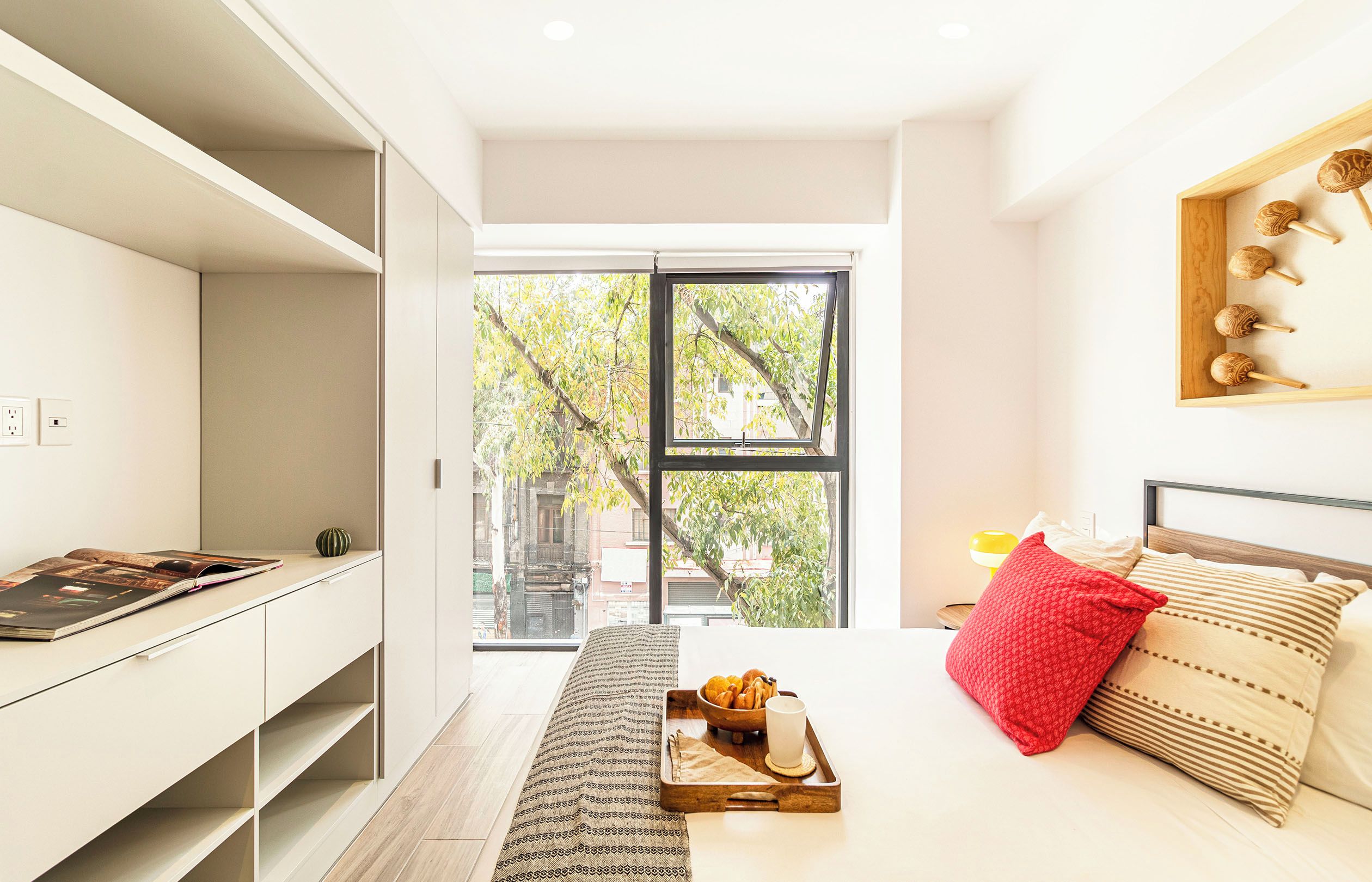 A modern bedroom with a bed, a bedside table, a window, and a view of trees outside.
