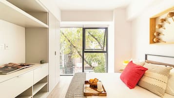 Un dormitorio moderno con cama, mesita de noche, ventana y vistas a árboles.