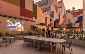 An outdoor dining area with a large table and chairs, surrounded by greenery and a colorful mural on the wall. - Kukun Reforma Downtown (Mexico City)
