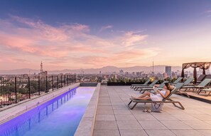 Un área de piscina en la azotea con sillones de descanso y vistas del horizonte de la ciudad.
