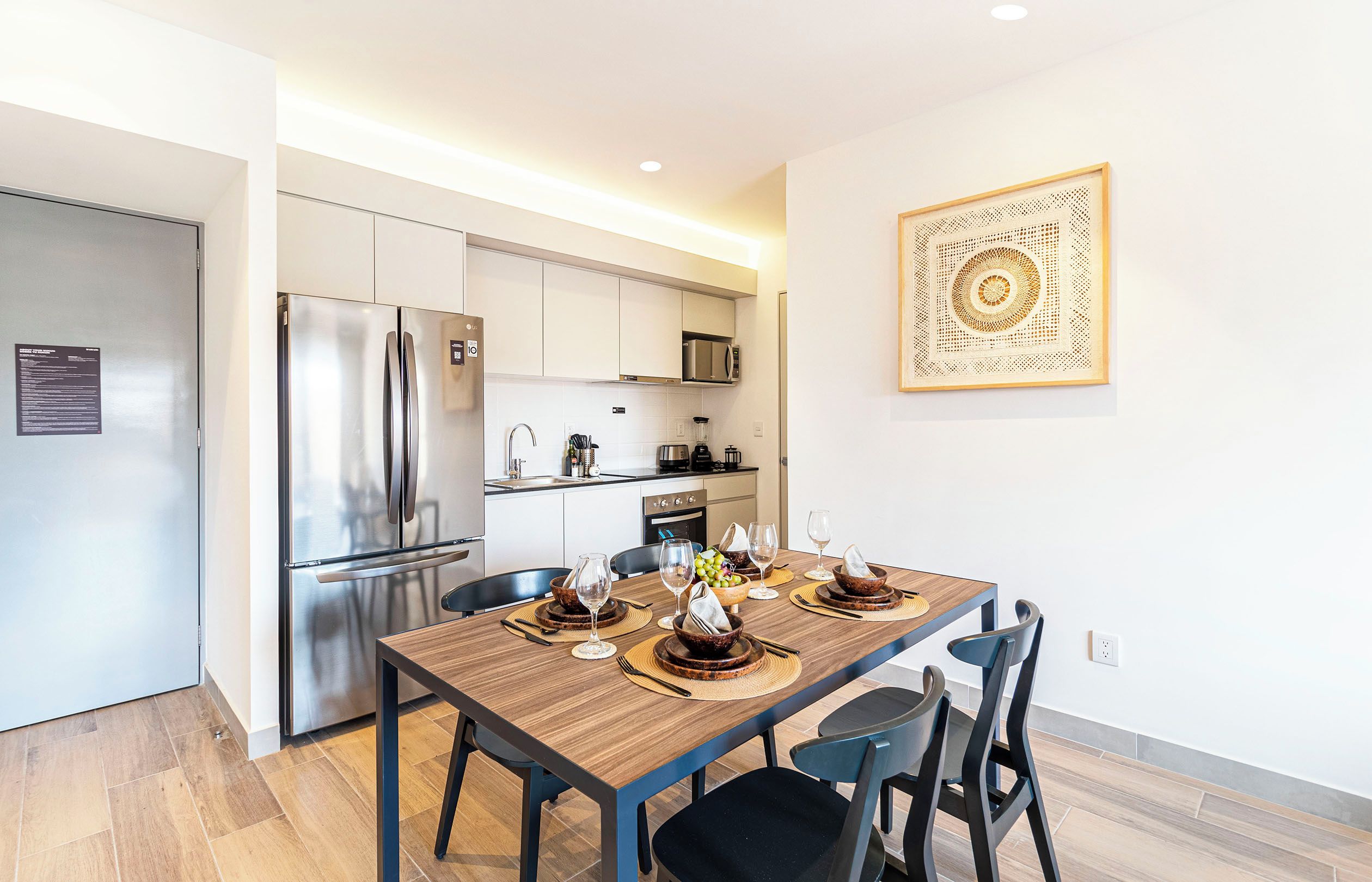 A modern kitchen with stainless steel appliances, a dining area with a wooden table and chairs, and a decorative wall piece.