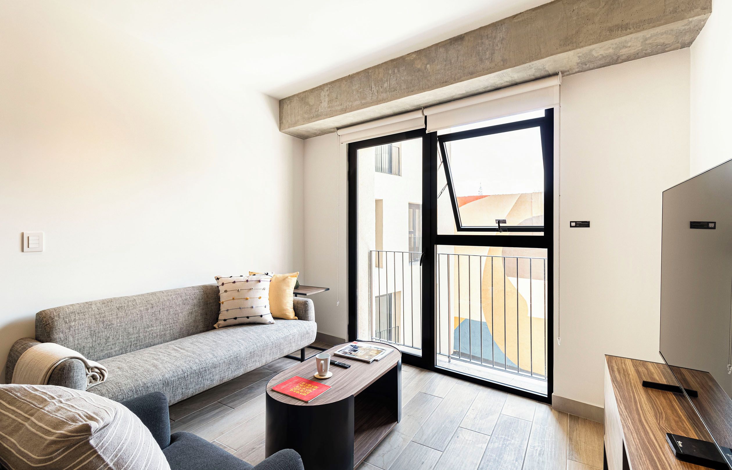Uma sala de estar moderna com um sofá cinza, uma mesa de centro com um livro e uma TV sobre um suporte de madeira.