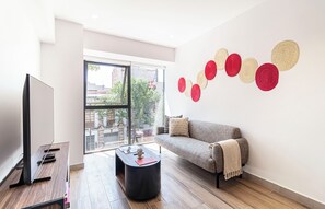 A modern living room with a flat-screen TV, a grey sofa, a coffee table, and a wall art installation. - Kukun Reforma Downtown (Mexico City)