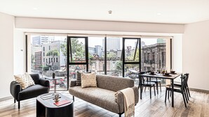 A modern living room with a sofa, armchair, and dining table, large windows with a city view, and wooden flooring. - Kukun Reforma Downtown (Mexico City)