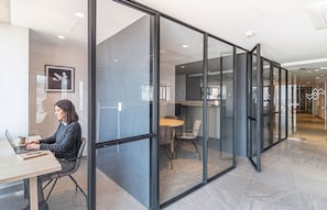 Un espacio de oficina con separaciones de vidrio, una persona trabajando en un escritorio y una vista panorámica de la ciudad a través del cristal.