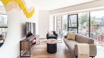 Una sala de estar moderna con sofá, mesa de centro, televisión y vista a la ciudad a través de amplios ventanales.