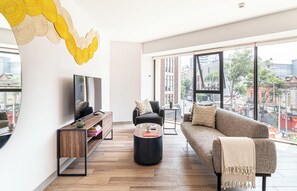 A modern living room with a sofa, coffee table, TV, and a city view through large windows. - Kukun Reforma Downtown (Mexico City)