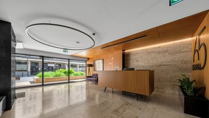 A modern reception area with a wooden reception desk, a brick wall, and a large window providing a view of the outdoors. - Warsaw Wola Studio - Balcony & Workspace -by Rentujemy (Warszawa)