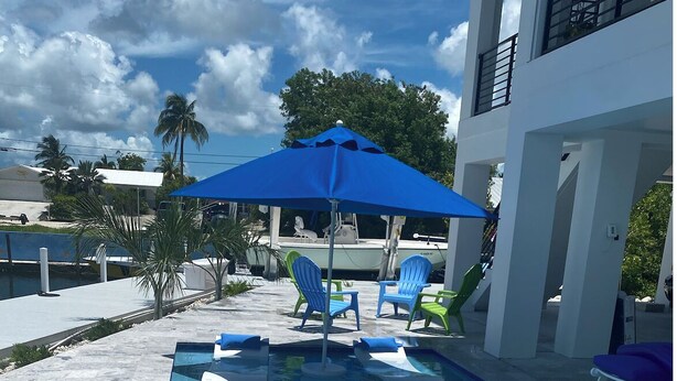 A swimming pool with clear blue water, surrounded by lounge chairs and a blue umbrella. - Gorgeous new build on Cudjoe Marina Basin with 80 ft boat dock and private pool (Cudjoe Key)