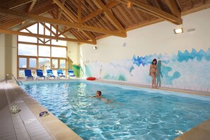 Una piscina interior con vigas de madera, un mural y vistas a montañas a través de amplios ventanales.