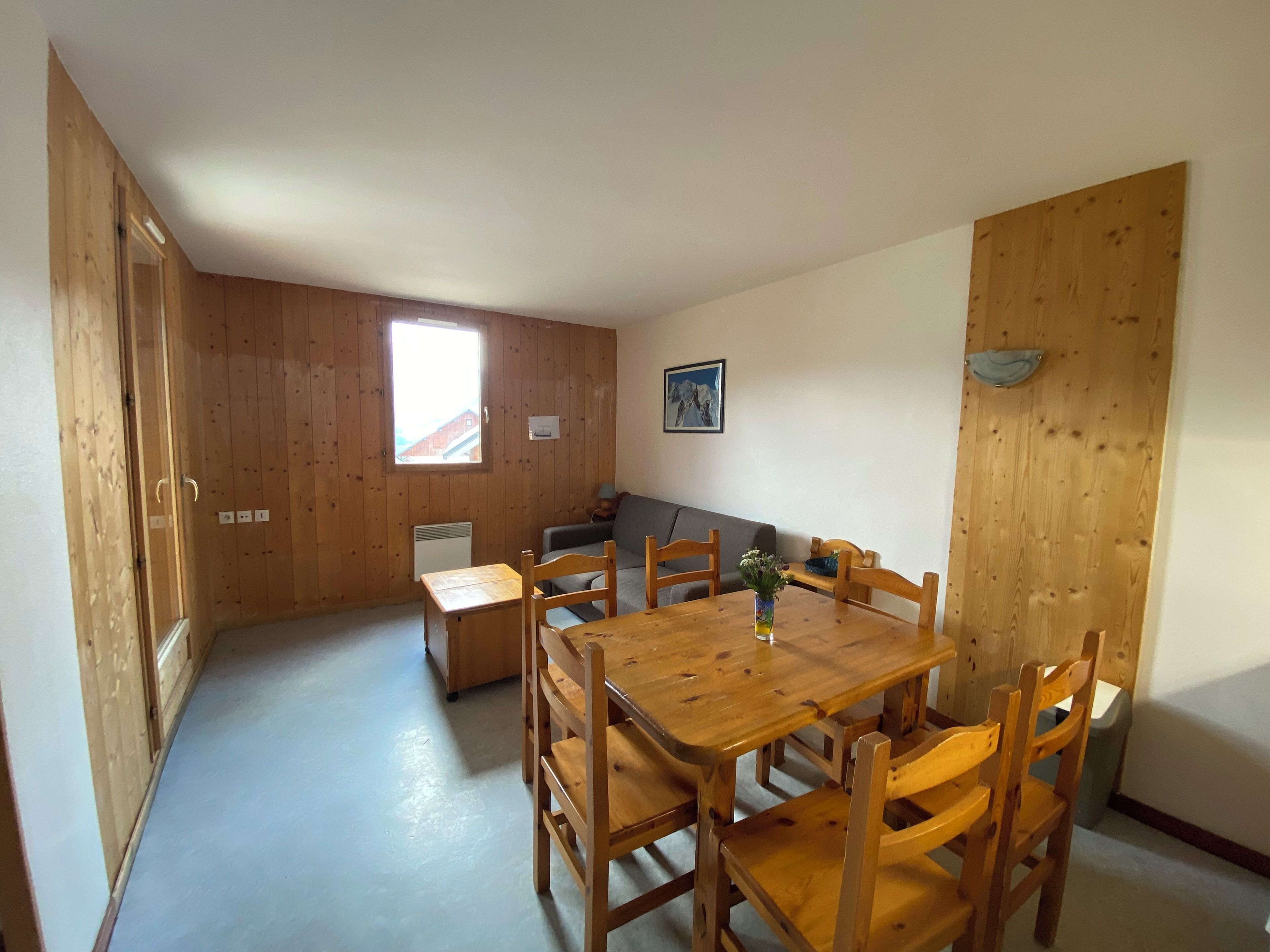 Um quarto com uma mesa de jantar de madeira e cadeiras, um sofá, uma janela e um quadro na parede.