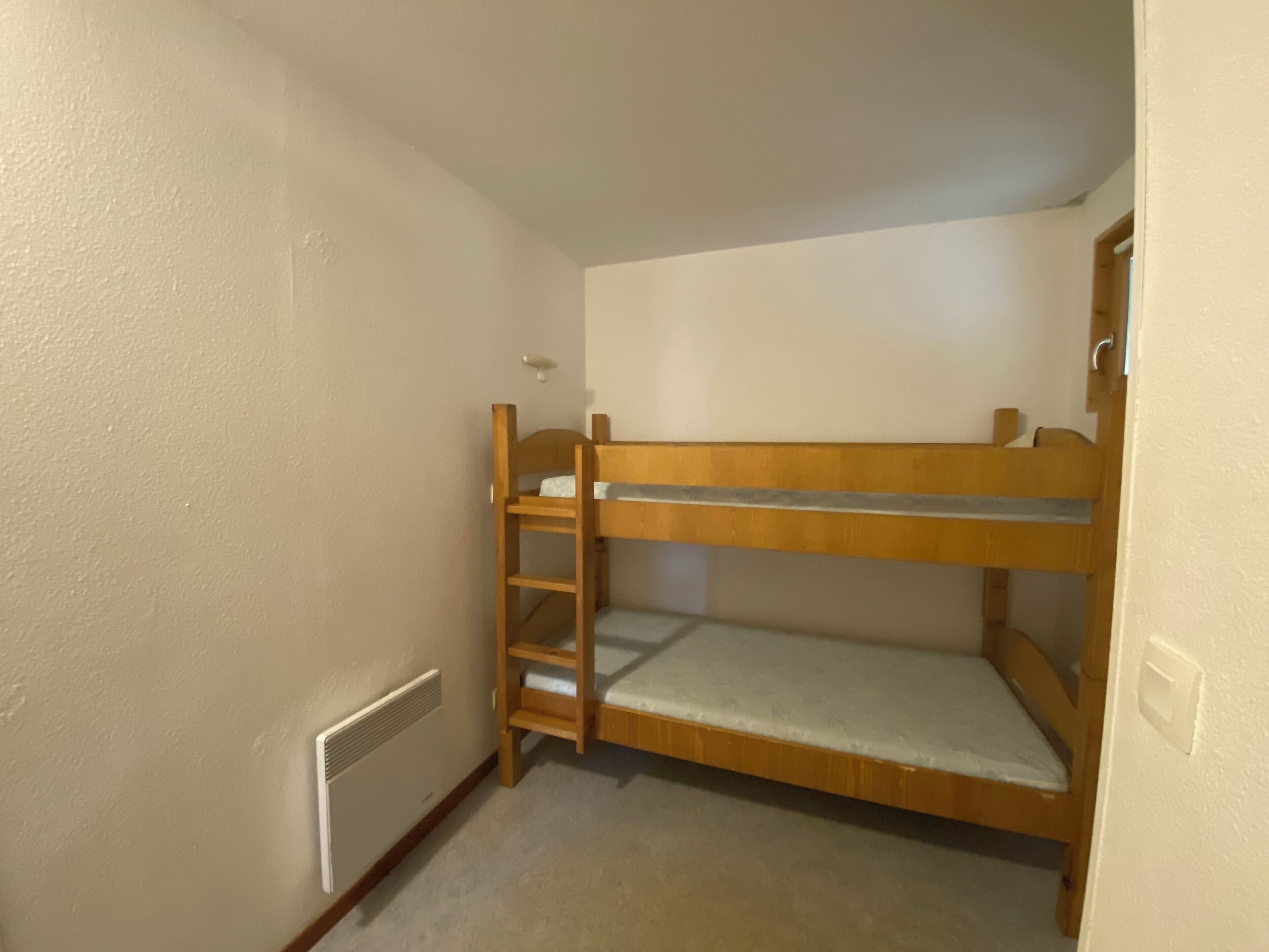 Ein Etagenbett in einem kleinen Raum mit weißen Wänden und einer Heizung.