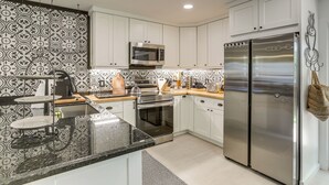 A modern kitchen with white cabinets, stainless steel appliances, and patterned backsplash. - Vibrant North Palm Beach Home ~ 2 Mi to Beach! (North Palm Beach)