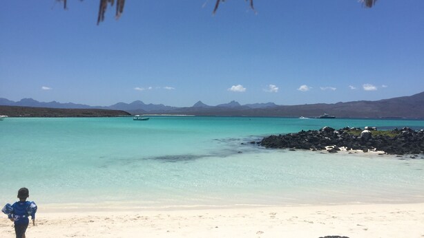 A beach with clear turquoise water, a child walking on the sand, and mountains in the background. - Studio Yuca - at Loreto 80 downtown  (Loreto)