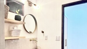 A bathroom with a round mirror, a wooden shelf with a potted plant, a round sink, and a hanging light fixture. - Studio Yuca - at Loreto 80 downtown  (Loreto)