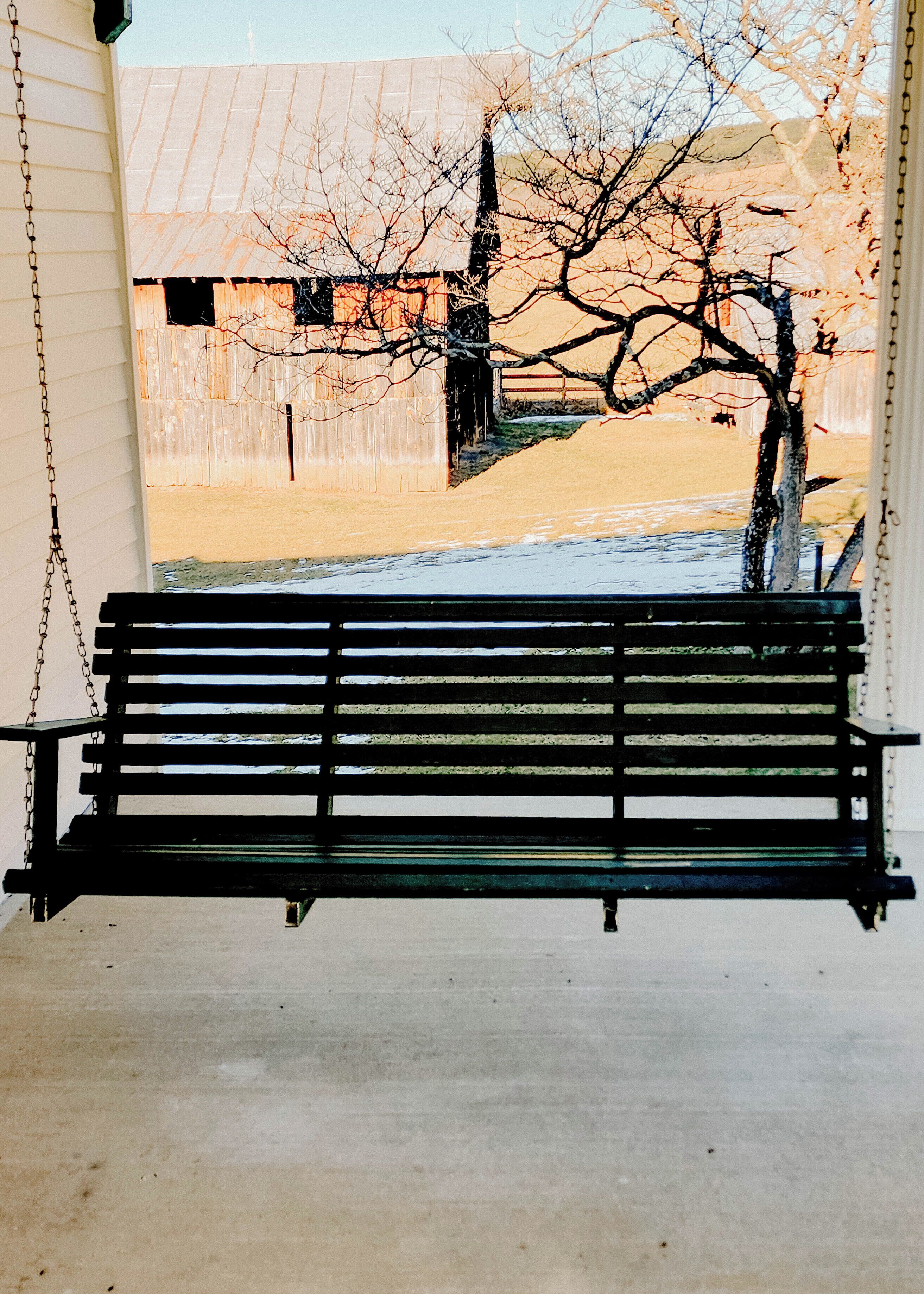 A black bench with metal chains on a porch.