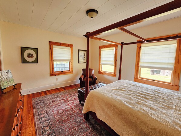 Un dormitorio con cama con dosel, suelo de madera y un amplio ventanal con persianas.