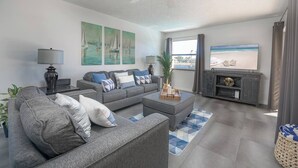 A modern living room with a grey sofa set, a coffee table, a TV, and artwork on the walls. - Waterfront Villa: Gulf Access Canal,  Dog Friendly, Heated Pool (Cape Coral)