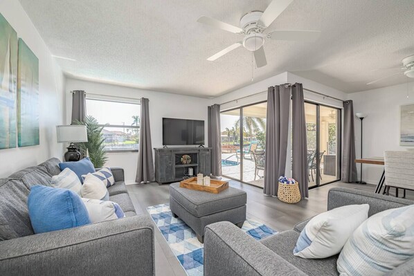 A modern living room with a grey sofa set, a flat-screen TV, and a ceiling fan.