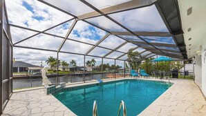 A covered swimming pool with a clear view of the surrounding area, including a boat dock and palm trees. - Waterfront Villa: Gulf Access Canal,  Dog Friendly, Heated Pool (Cape Coral)