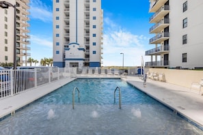 Une piscine à l’eau d’un bleu cristallin, entourée de clôtures blanches et jouxtant un immeuble à plusieurs étages doté de balcons.