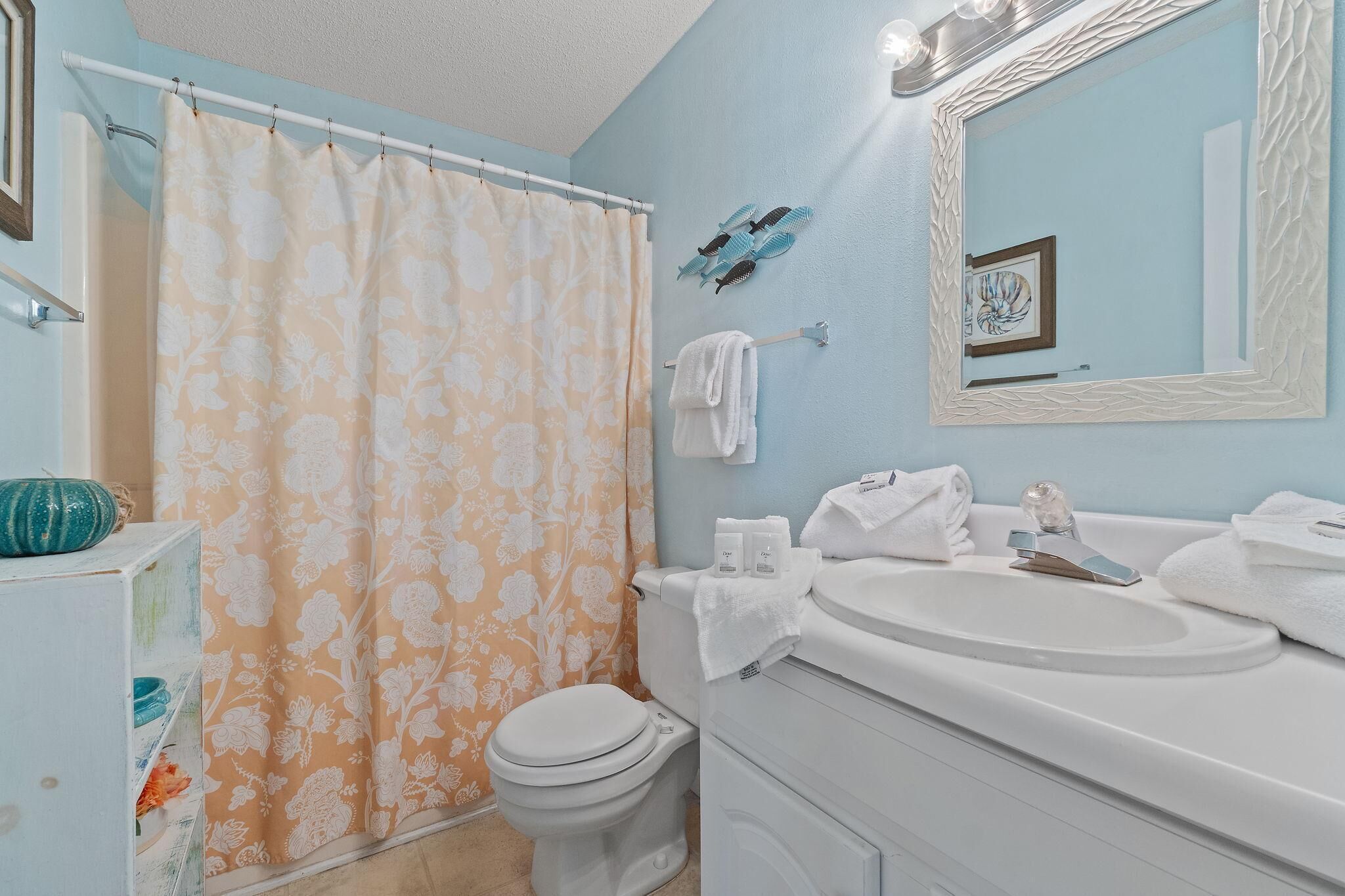 A bathroom with a shower curtain, toilet, sink, and towel rack.