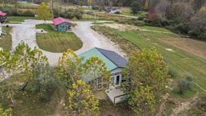 A rural property with a green-roofed building, a dirt path, and surrounding vegetation. - OSU Camper/RV (New Lexington)