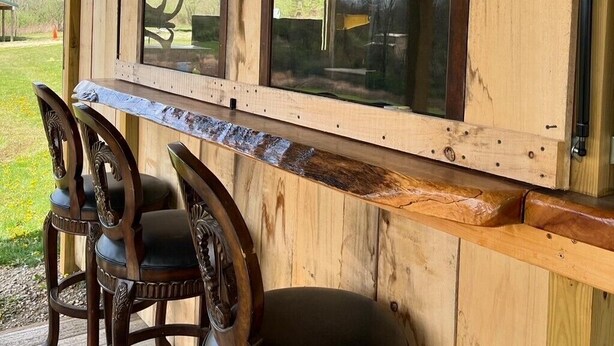 A wooden bar area with a view of the outdoors, featuring a wooden counter and three chairs. - OSU Camper/RV (New Lexington)