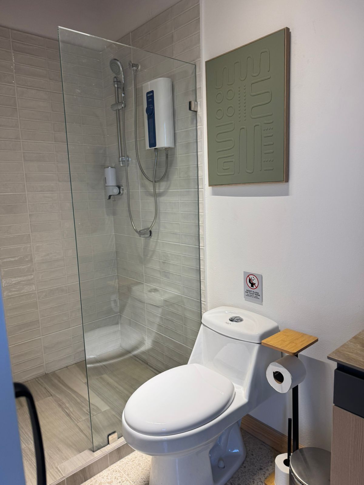 Une salle de bain moderne avec une douche à parois de verre, des toilettes dotées d’un porte-serviettes en papier et une étagère en bois.