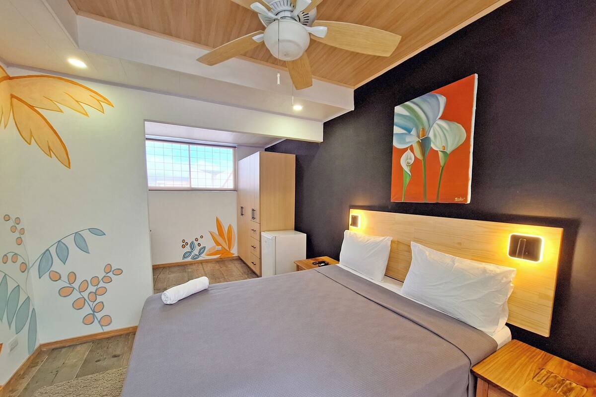 Una habitación de hotel moderna con una cama grande, cabecera de madera y un ventilador de techo.