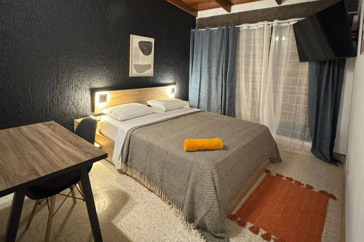 Un dormitorio con una cama, un escritorio, un ventilador de techo y un televisor montado en la pared.