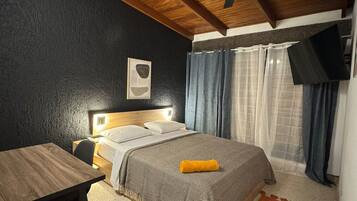 Un dormitorio con una cama, un escritorio, un ventilador de techo y un televisor montado en la pared.