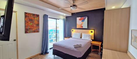 A modern bedroom with a bed, bedside tables, a desk, a ceiling fan, and artwork on the walls.