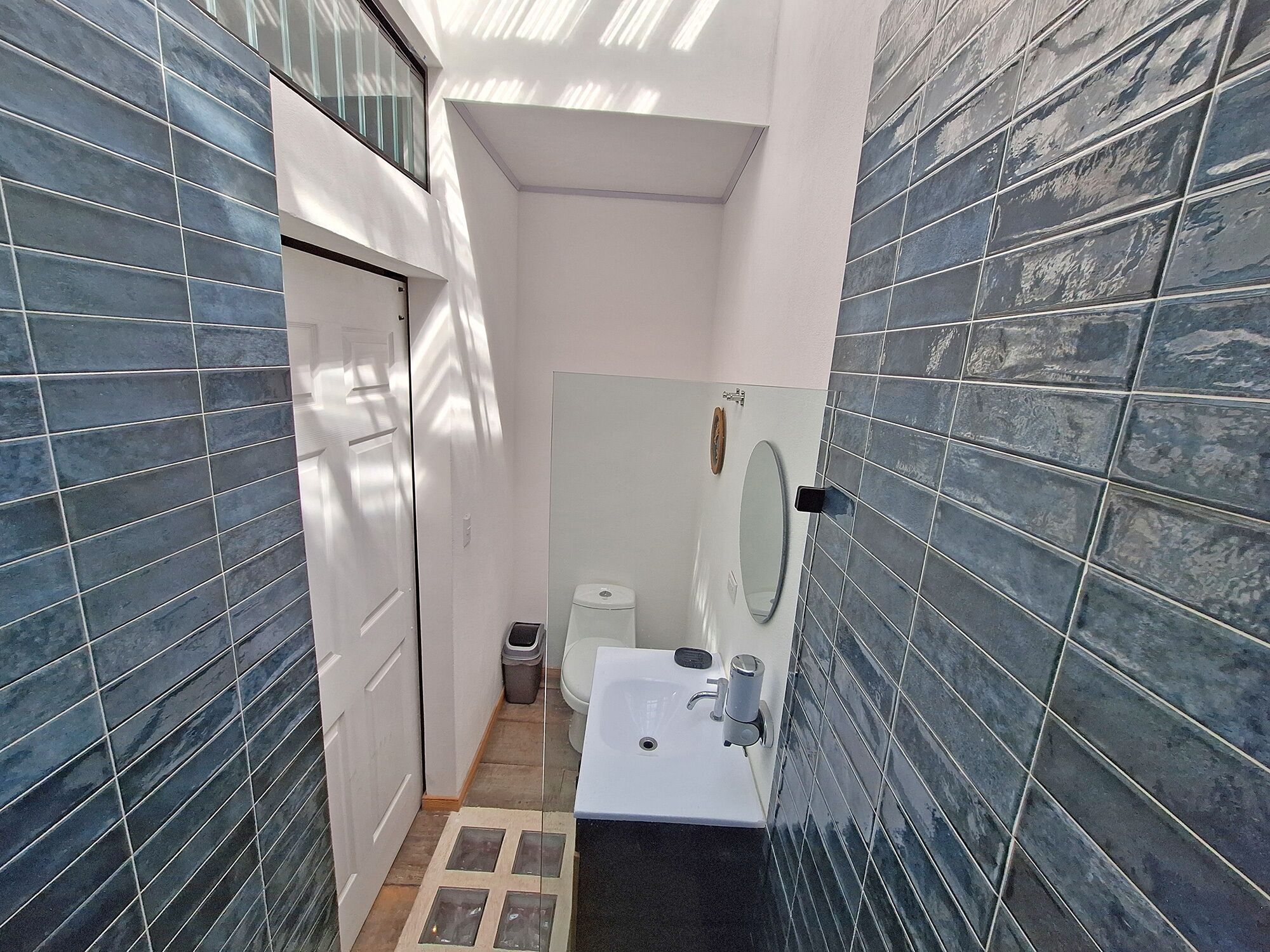 A narrow bathroom with blue-tiled walls, a white sink, and a mirror.