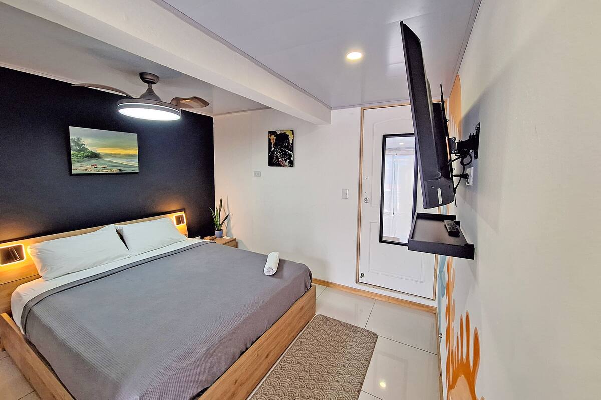 Un dormitorio moderno con cama, ventilador de techo, obra de arte y televisor montado.