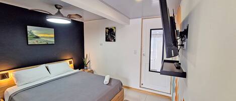 A modern bedroom with a bed, ceiling fan, artwork, and a mounted TV.