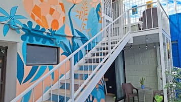 A staircase leading to a balcony with a colorful mural, a small table with a potted plant, and a window with a black frame.