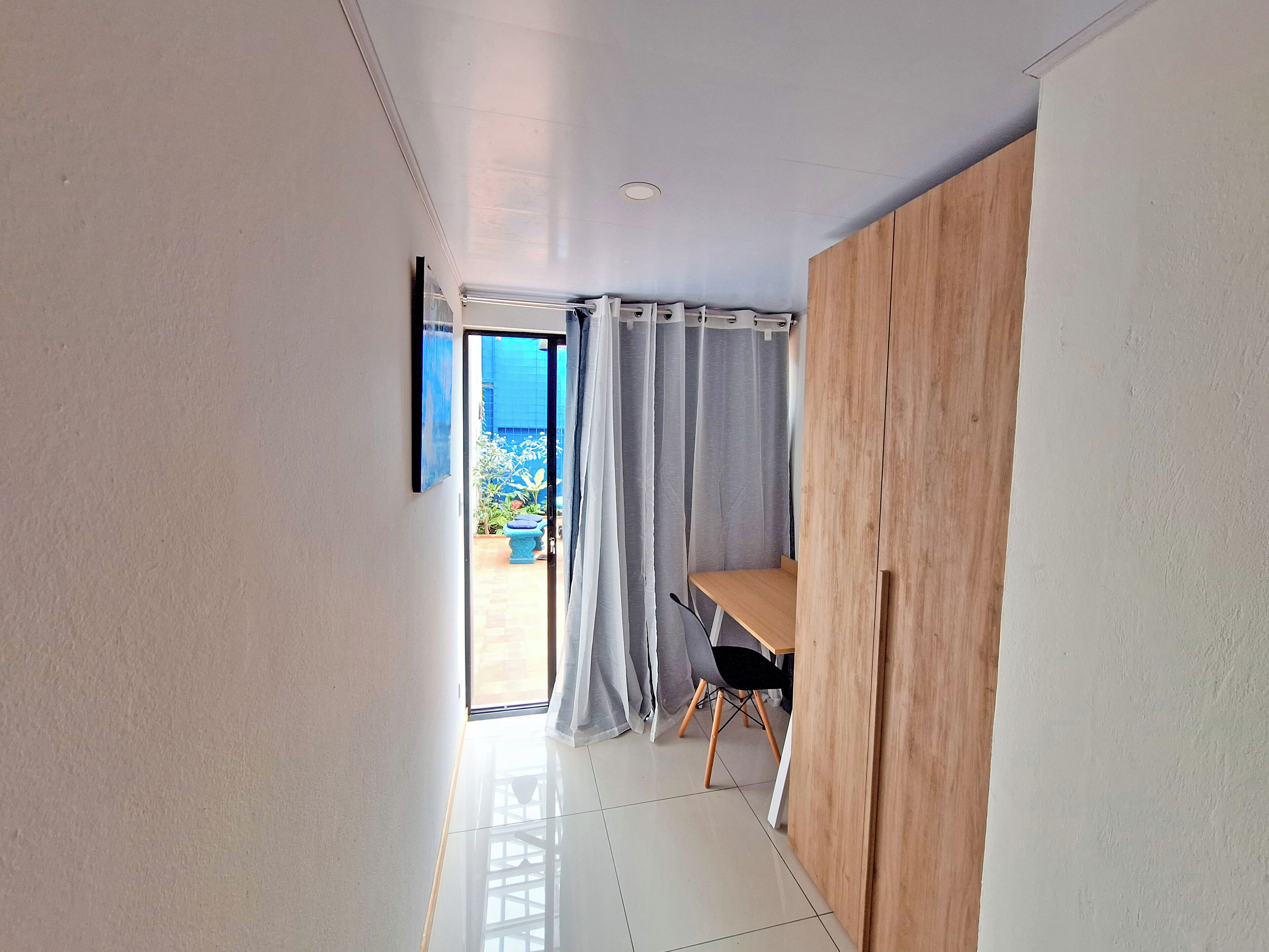 A modern room with a wooden desk, a chair, and a view through a glass door to an outdoor area with plants.