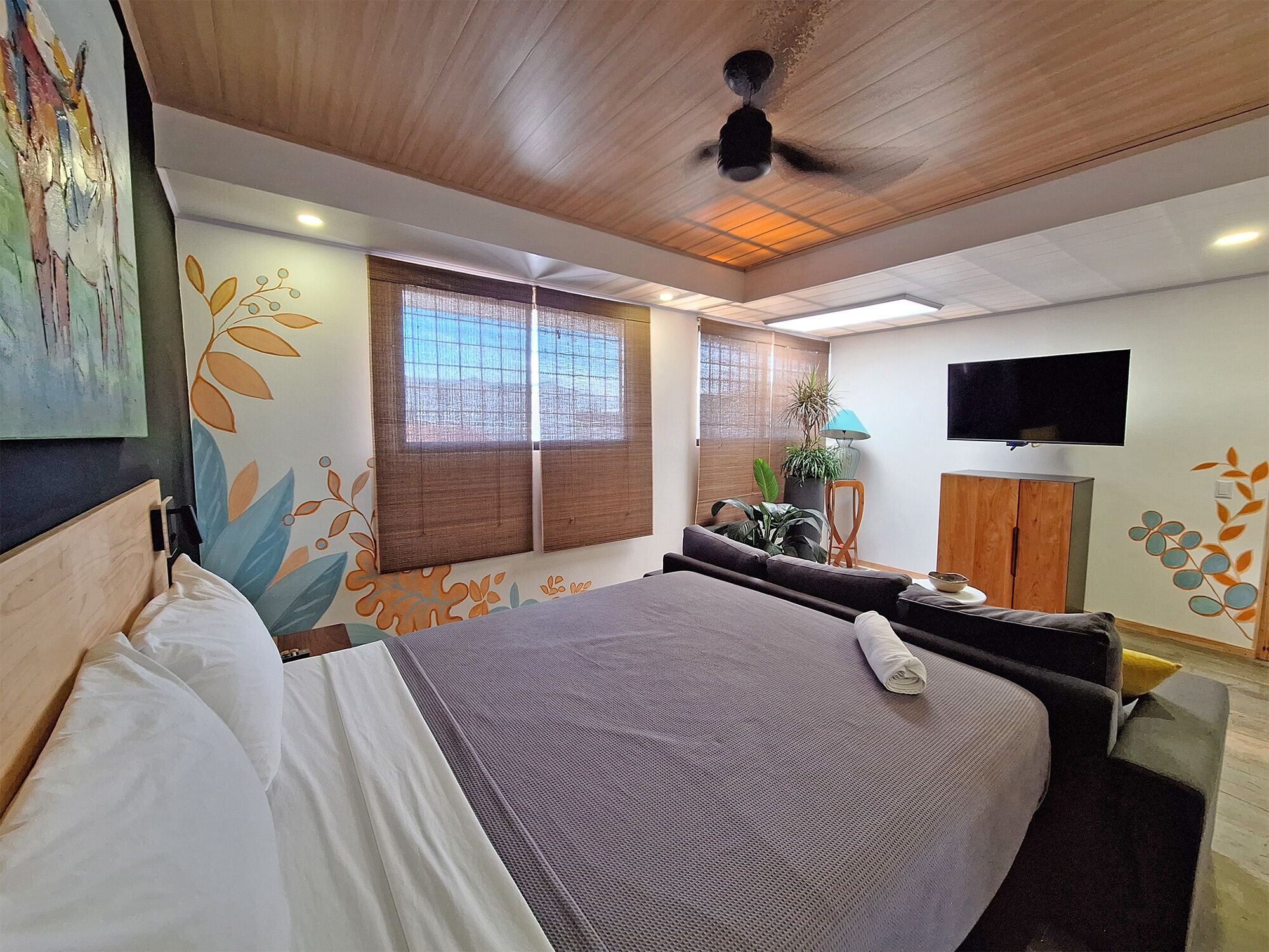 A bedroom with a bed, a TV, a desk, and a window with blinds.