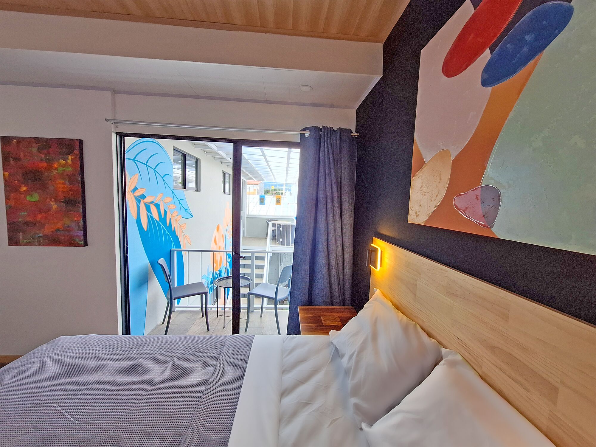 A hotel room with a bed, a view of the balcony, and a painting on the wall.