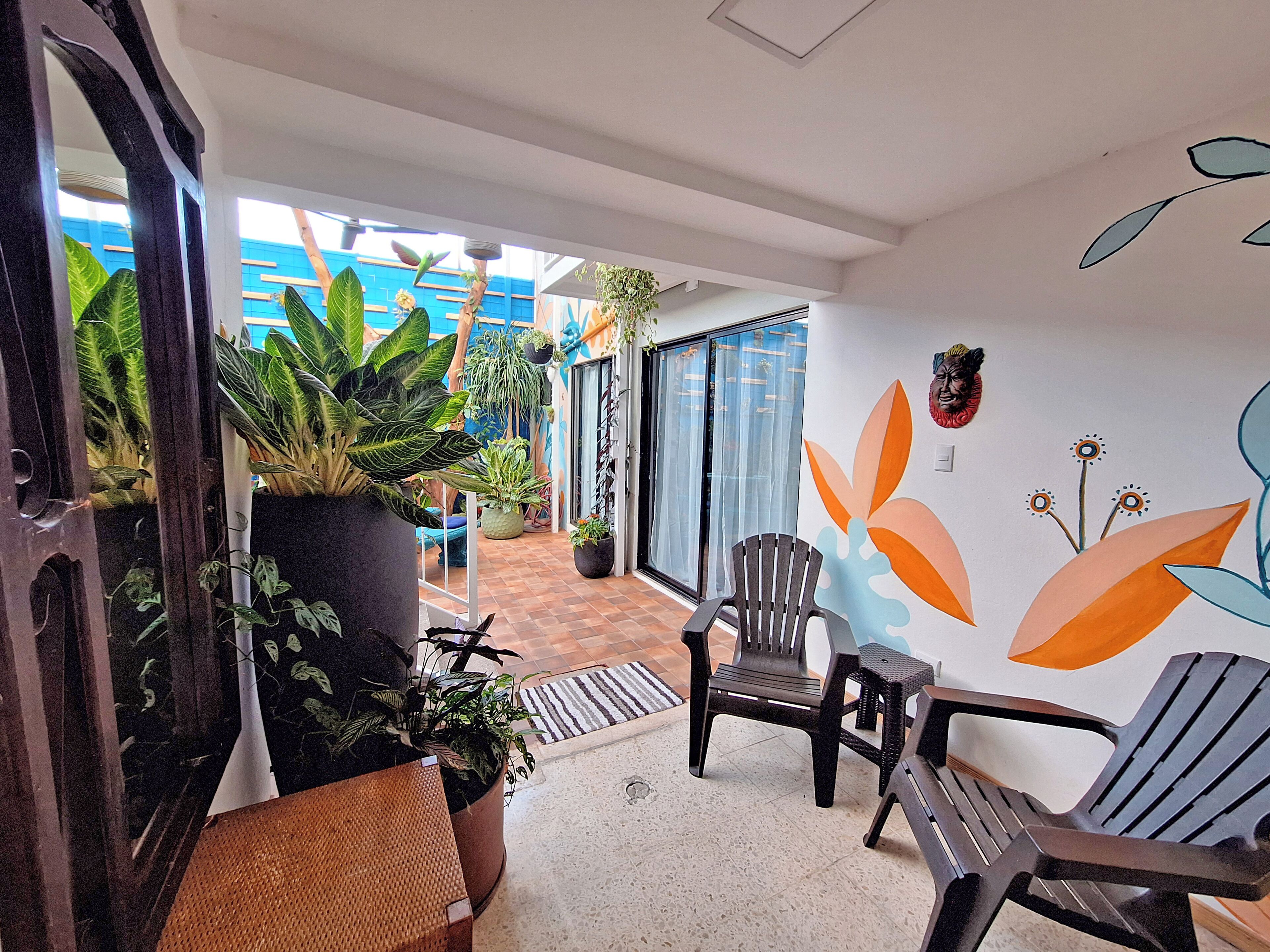An indoor seating area with potted plants, a wall mural, and a view of the outside.