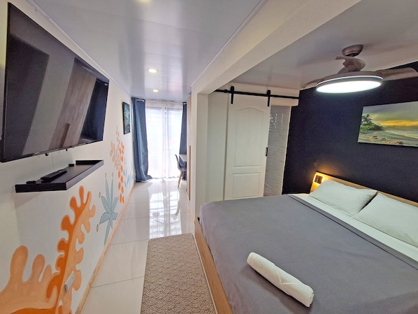 Una habitación de hotel moderna con una cama, un televisor montado en la pared, un ventilador de techo y un cuadro.