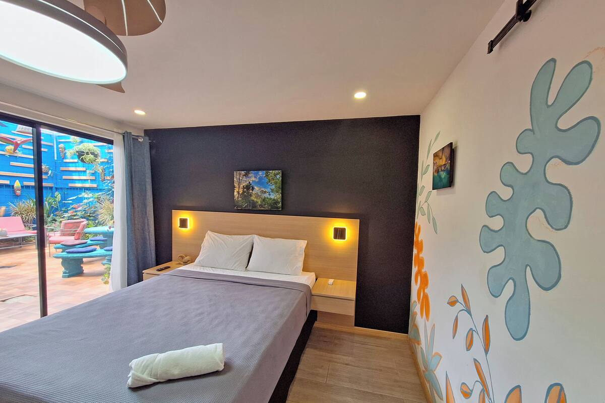 Una habitación de hotel moderna con una cama grande, una mesita de noche y una lámpara de pared.
