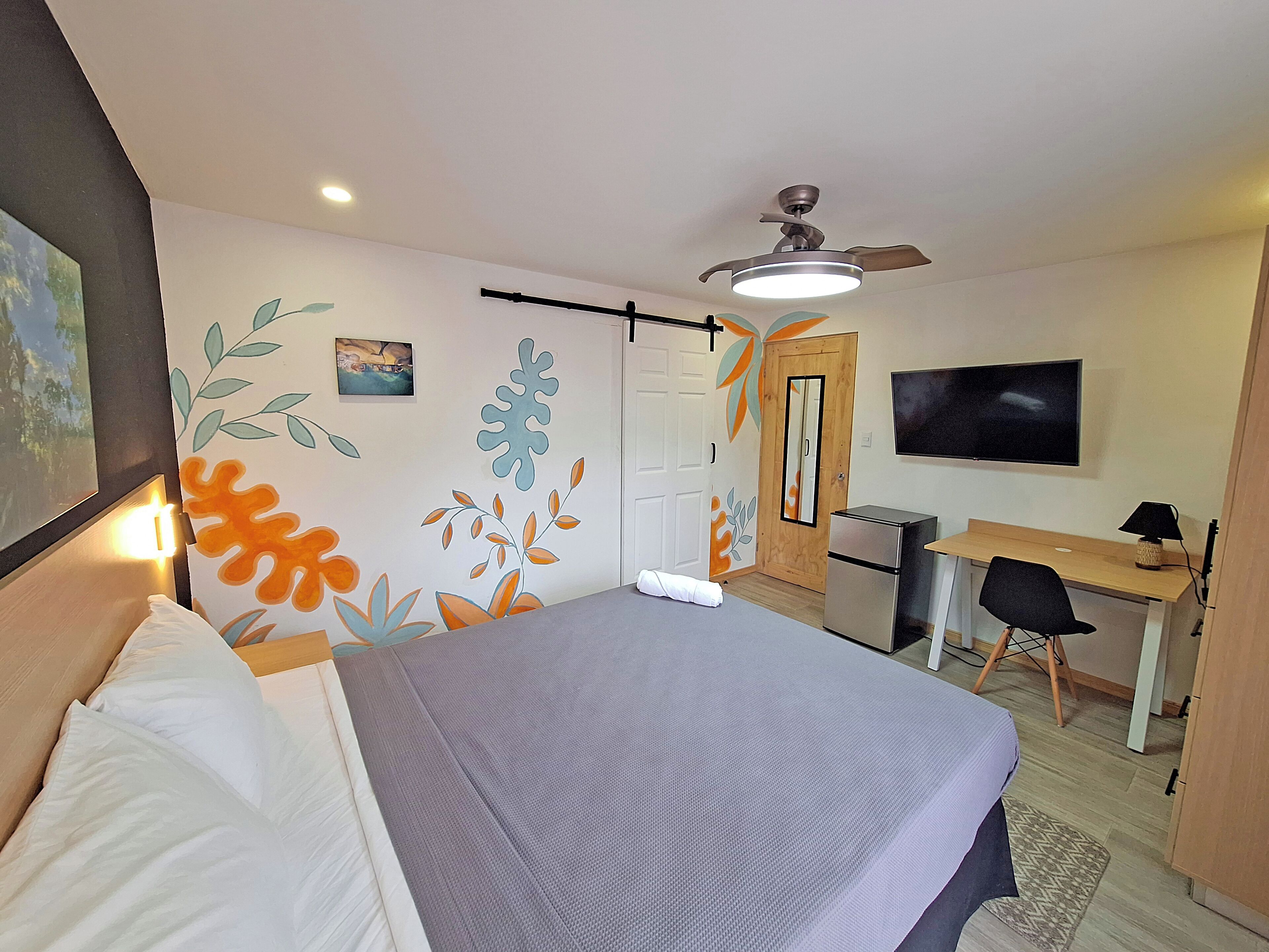 A hotel room with a bed, desk, chair, TV, and a ceiling fan.