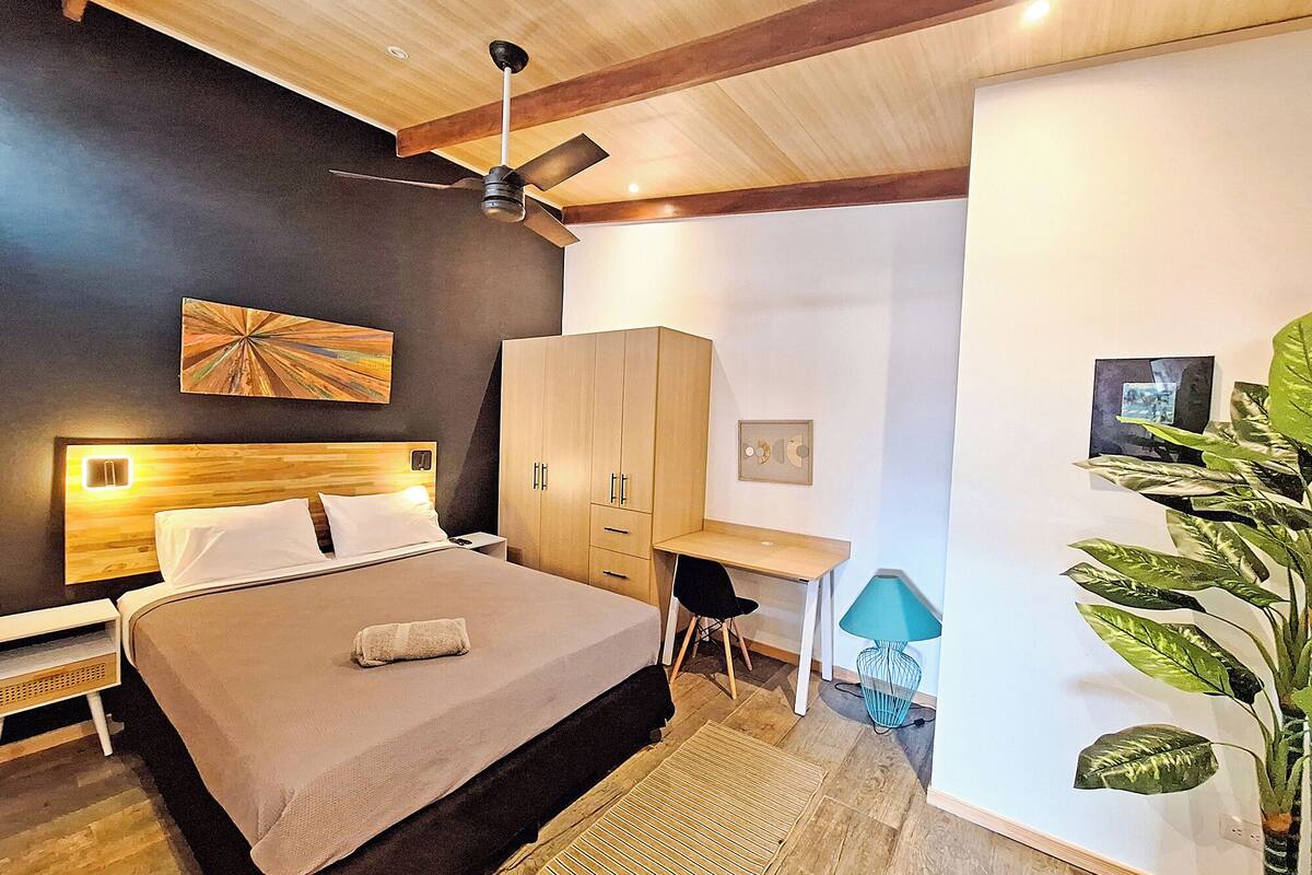 Un dormitorio moderno con cama, escritorio, armario y ventilador de techo.