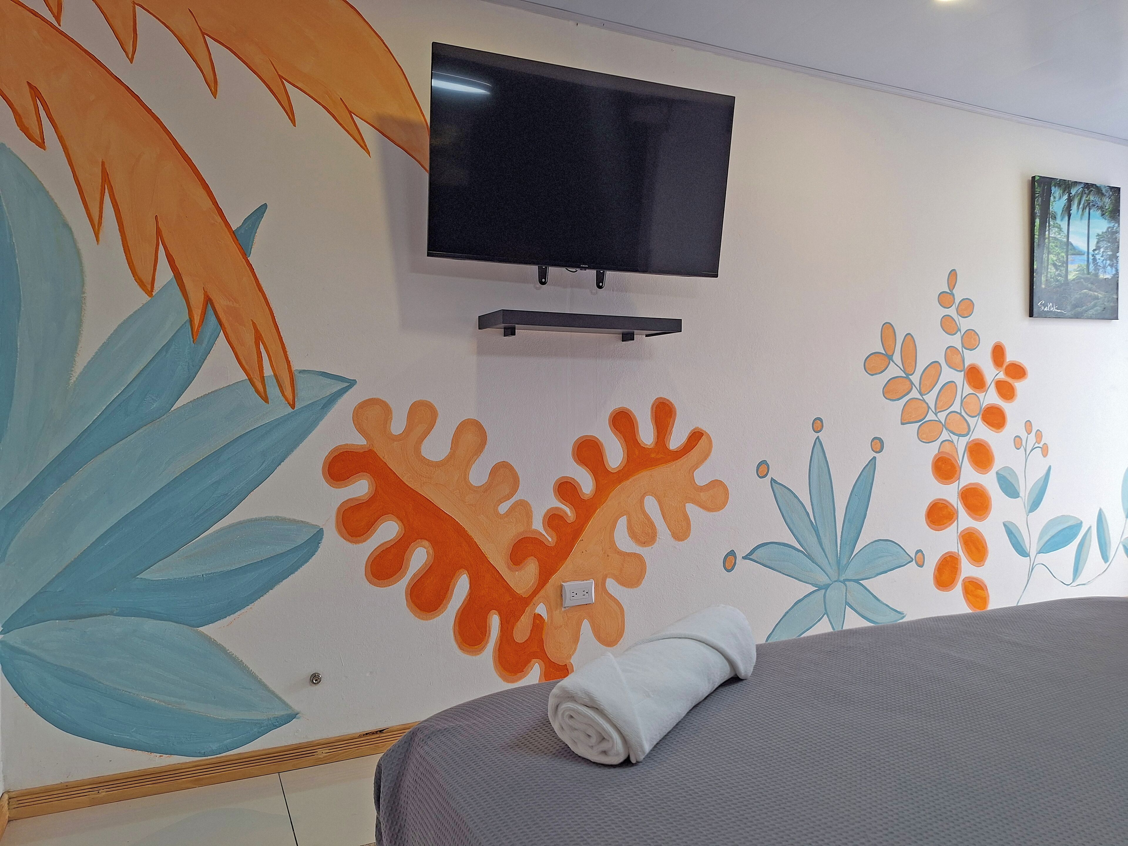 A hotel room with a bed, a TV mounted on the wall, and a colorful mural on the wall.