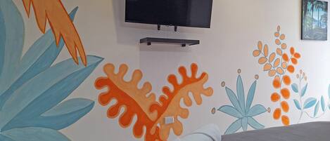 Una habitación de hotel con una cama, un televisor montado en la pared y un mural colorido.