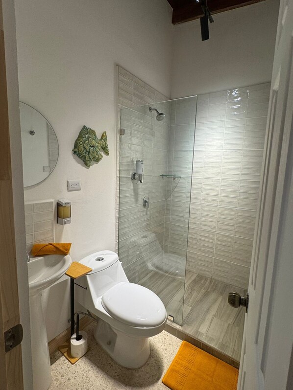 Un baño moderno con inodoro, lavamanos y cabina de ducha con mampara de vidrio.